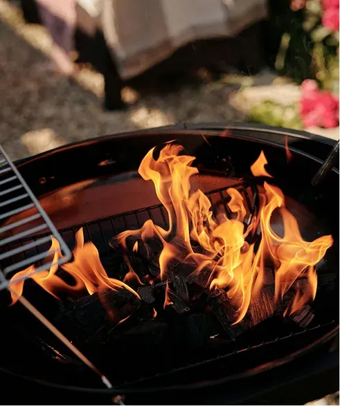 Close-up of orange flames rising from charcoal in a round grill with a cooking grate