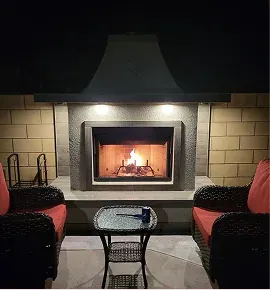 Outdoor fireplace with tile surround and two red-cushioned wicker chairs